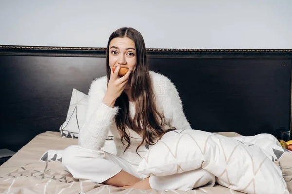 Encantadora chica de pelo largo se sienta en la cama, desayunos una deliciosa manzana útil — Foto de Stock