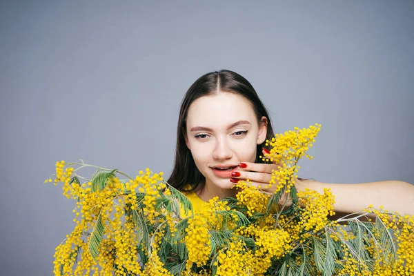 Uma jovem menina de luxo sorri segurando uma mimosa amarela perfumada — Fotografia de Stock
