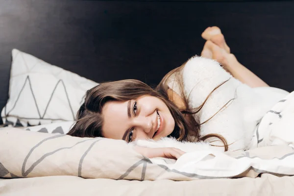 Linda chica somnolienta se encuentra en la cama, quiere dormir y sonríe — Foto de Stock