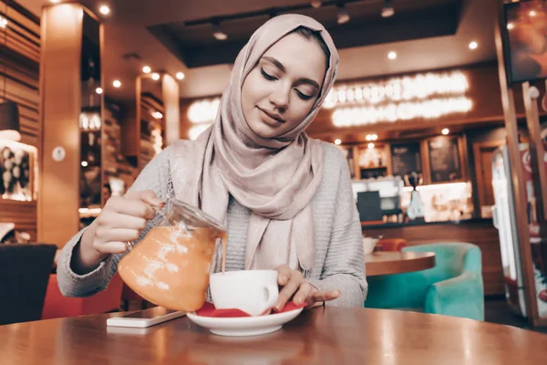 Agradable chica árabe en hijab se sienta en un acogedor café, bebe té fragante y descansa —  Fotos de Stock