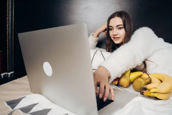 Mooie langharige meisje ligt op bed en interessante film kijkt op haar laptop — Stockfoto