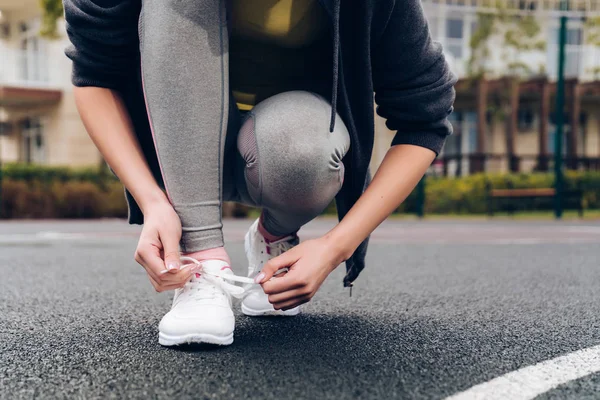 Спортивна молода дівчина зв'язує свої туфлі на кросівках, поїздах на спортивному майданчику — стокове фото