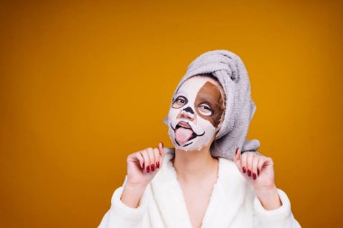 garip bir genç kız başını ve beyaz bornoz havlu ile dilini, yüzünde bir maske ile bir köpeğin yüzünü gösterir