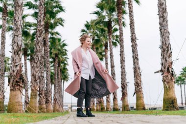 yanındaki uzun boylu yeşil palms bir bahar parkta yürüyüş pembe bir ceket şık genç kız