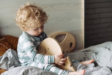 tahta oyuncakla oynamak yatakta oturup şirin küçük kıvırcık oğlu