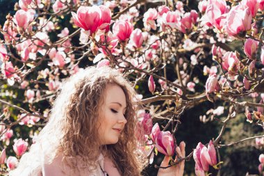 Bahar ve sıcaklık zevk bir parkta blooming pembe Manolya karşı poz kıvırcık zarif kız