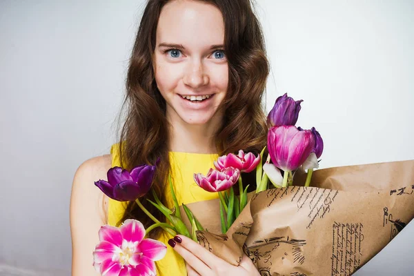 Glad ung blåögda flicka i en gul klänning som håller en bukett doftande blommor — Stockfoto