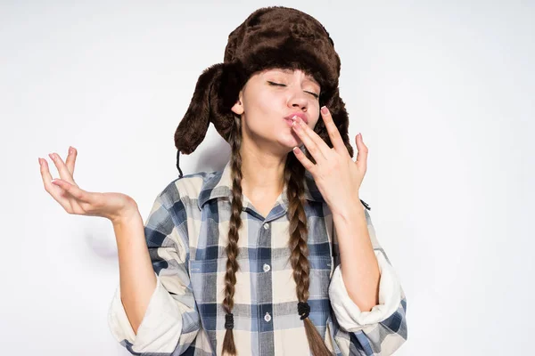 A young hungry Russian girl in a fur hat eats delicious hot pancakes on Shrovetide — Stock Photo, Image