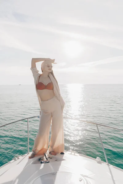 Elegante ragazza in abiti estivi alla moda in posa sul suo yacht bianco al sole — Foto Stock