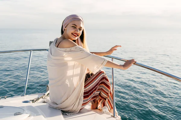 Ő fehér jacht a nap és a mosoly ül boldog gazdag lány, divatos nyári ruha — Stock Fotó