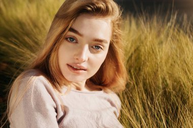 Genç sarışın mavi gözlü kız çim alanda yatıyor ve kameraya doğru görünüyor