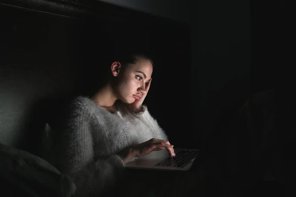 Laptop seyir yorgun yorgun kız yatakta, karanlıkta, gece geç saatlerde, oturma — Stok fotoğraf