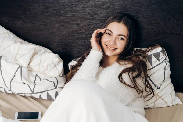 Linda menina com cabelos longos encontra-se na cama no início da manhã, sorrindo e desfrutando de um bom dia — Fotografia de Stock