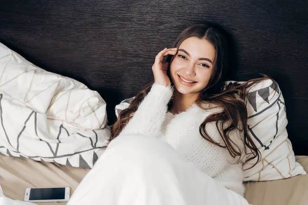 Chica encantadora con el pelo largo se encuentra en la cama temprano en la mañana, sonriendo y disfrutando de un buen día — Foto de Stock