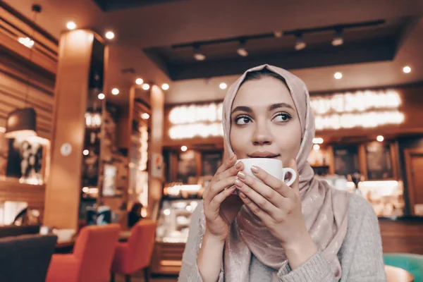 Süße junge Muslimin im Hijab sitzt im Café und trinkt duftenden Kaffee — Stockfoto