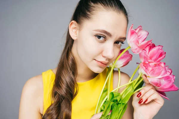 Attractive elegant girl in yellow dress holds fragrant flowers and looks at camera — Stock Photo, Image