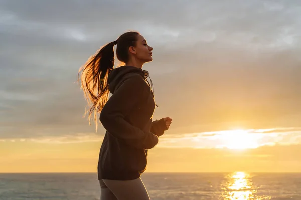 Självsäker långhåriga flicka löper längs banvallen vid solnedgången, förbereda för tävlingar — Stockfoto