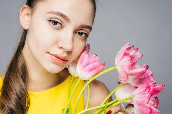 Güzel genç kız model sarı elbiseli güzel kokulu pembe çiçekler tutar, kamera ve pozlar görünüyor — Stok fotoğraf