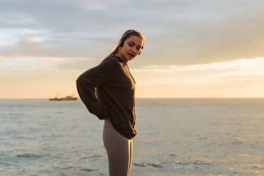kulaklıklar müzik dinlerken huzurlu genç kız deniz kenarında, koşu sonra dinlenme