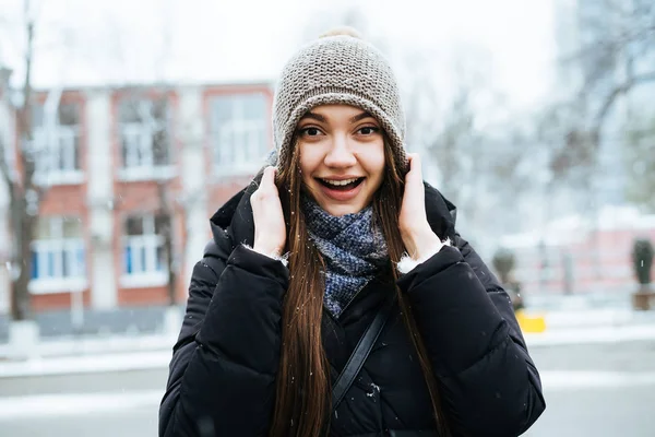Schöne glückliche Mädchen mit einem warmen Winterhut geht durch die Straßen der Stadt bei kaltem Winterwetter und lächelt — Stockfoto