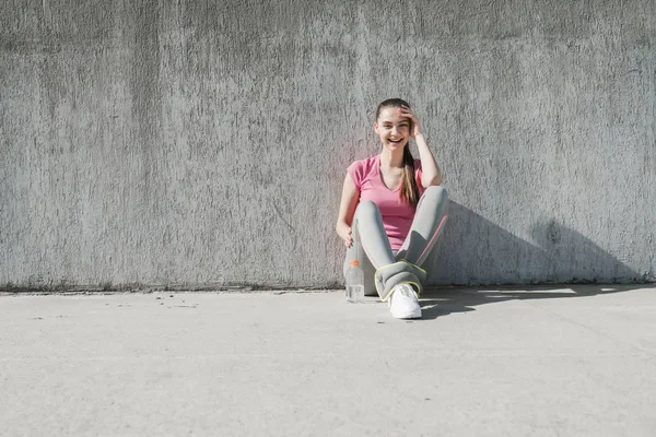 Cute młoda dziewczyna siedzi na ziemi na zewnątrz, odpoczynek po szkoleniach i rośnie w siłę — Zdjęcie stockowe