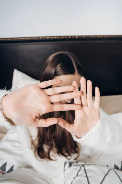 Schläfriges junges Mädchen sitzt im Bett, schließt das Gesicht mit den Händen und will nicht aufstehen — Stockfoto