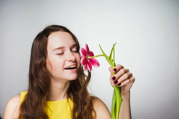 Niedliche junge Mädchen in einem gelben Kleid lächelt und riecht eine duftende Blume — Stockfoto