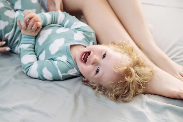 Malý kudrnatý chlapeček ležel na posteli vedle Mami, směje se — Stock fotografie