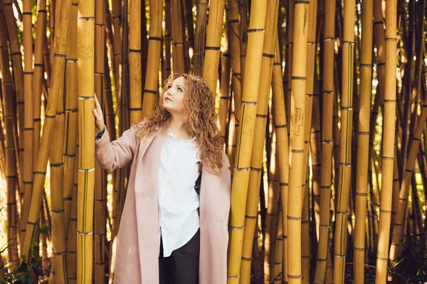 Curly elegant woman posing next to bamboo deerviami in park, resting — Stock Photo, Image