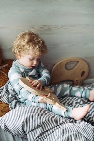 Маленький милий кучерявий хлопчик сидить у ліжку і грає зі своєю іграшкою — стокове фото