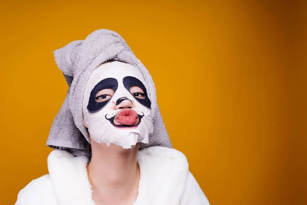 Funny mladá dívka s ručníkem na hlavě chce být krásná, na obličejovou masku s tváří panda — Stock fotografie