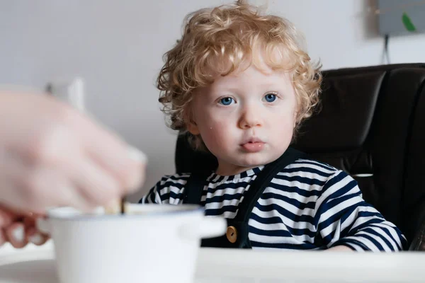 Curly little baby boy eating breakfast cereals, family breakfast — стоковое фото
