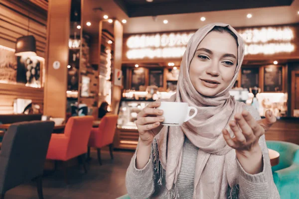 Une élégante fille musulmane avec un foulard assis dans un beau restaurant confortable et boire du café parfumé — Photo