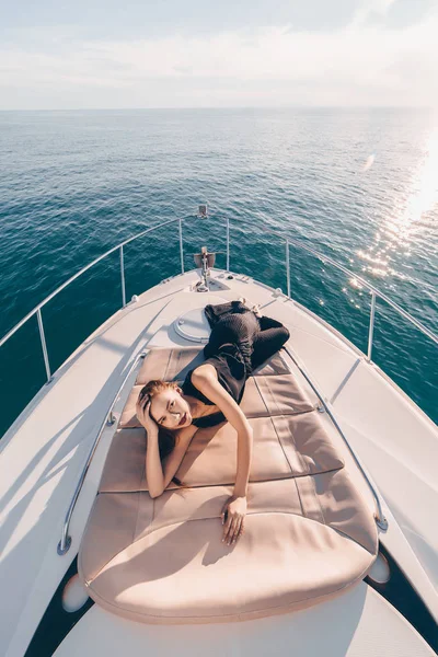 An attractive young woman in black summer clothes lies on her yacht, enjoys a luxurious life and the sea — Stock Photo, Image