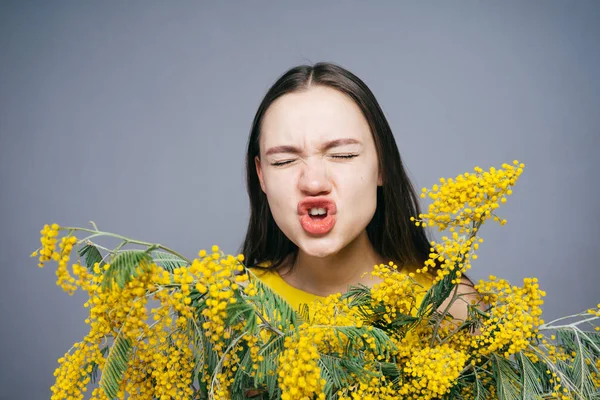 Młoda dziewczyna trzyma mimosa żółty i kicha, uczulenie na kwiaty — Zdjęcie stockowe