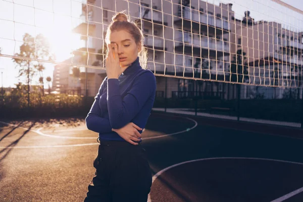 Elegante ragazza modello biondo in maglione blu in posa sul campo sportivo all'aperto al sole — Foto Stock