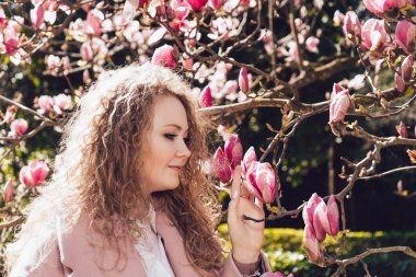 çiçek açan Manolya ve sıcak bahar hava kokusu tadını paltolu kıvırcık güzel kadın