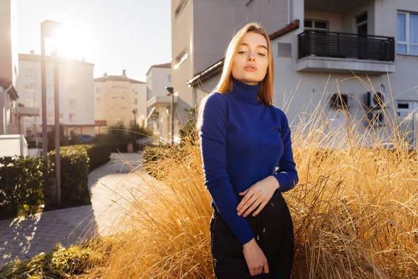 Mooi stijlvol meisje blond model in blauwe trui poseren op de straten van de stad in de zon — Stockfoto