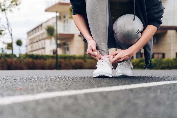 Una giovane ragazza lega i lacci delle scarpe da ginnastica, si allena su un campo sportivo all'aperto — Foto Stock