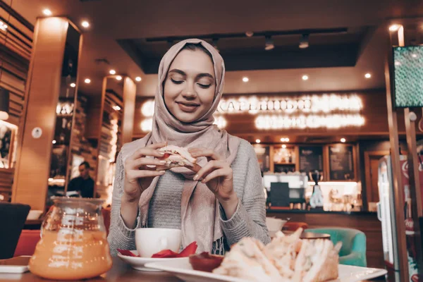 Aranyos lány muszlim fejkendőt ül egy hangulatos étterem és vacsora, mosolyogva — Stock Fotó