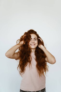 Liseli kız gülüyor ve elleriyle saçlarını topallıyor. parlak stüdyo