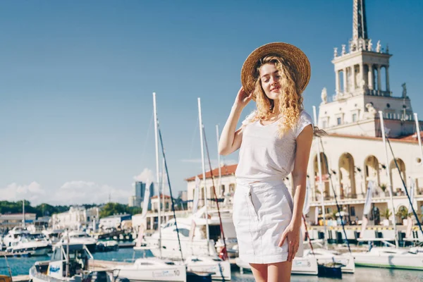 Chica en ropa blanca coqueta se pone de pie sobre el fondo de la terminal del mar y barcos —  Fotos de Stock