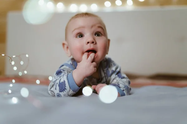 Barnet i kläder ligger på magen och håller fingrarna i munnen — Stockfoto