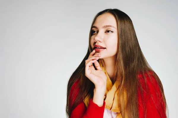 Una ragazza con rossetto luminoso e una camicetta rossa guarda con interesse e tiene il mento con la mano. luminoso studio — Foto Stock