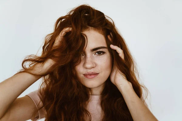 O estúdio é cinza claro. menina com um sorriso de desprezo olha para a câmera e baba o cabelo — Fotografia de Stock