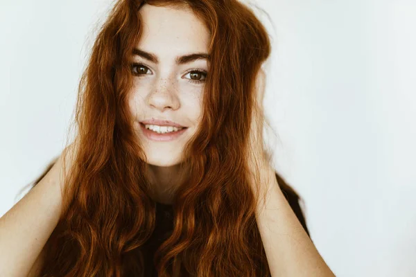 Bellezza luminosa in studio, scopandosi i capelli con le mani e sorridendo splendidamente — Foto Stock