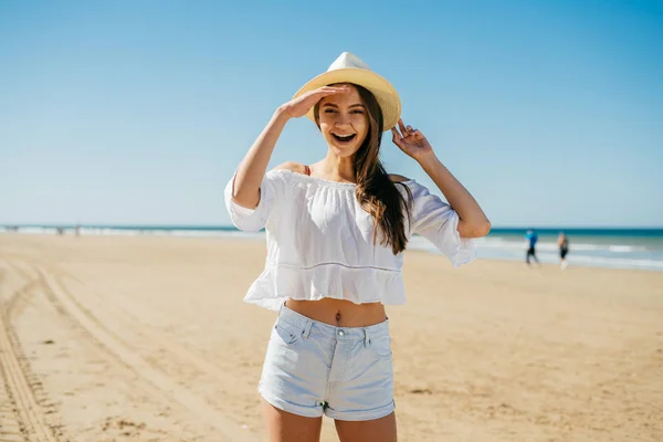 La ragazza col cappello con i capelli guarda gioiosamente qualcuno sulla spiaggia. Emozione di riconoscimento — Foto Stock