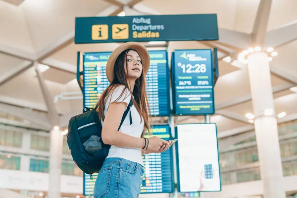 Young traveler at the airport on the background of the scoreboard carefully looking for something — Stock Photo, Image