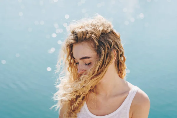 Czuła kręcona blondynka spoglądająca w dół siedzi na parapecie plaży naprzeciwko oceanu — Zdjęcie stockowe