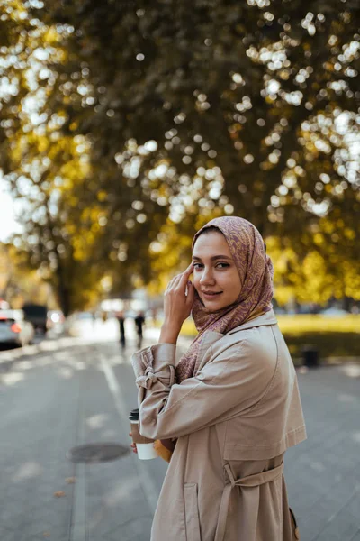 Muslim woman on a city street holds coffee and looks over her shoulder — Stock Photo, Image